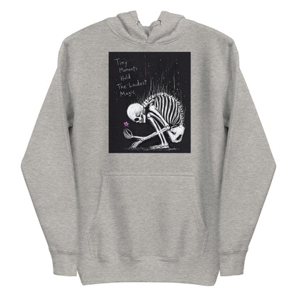 Carbon grey pullover hoodie with the 'Tiny Moments' goth graphic: a kneeling skeleton holding a tiny pink flower on a black background, with the words "Tiny moments hold the loudest magic"