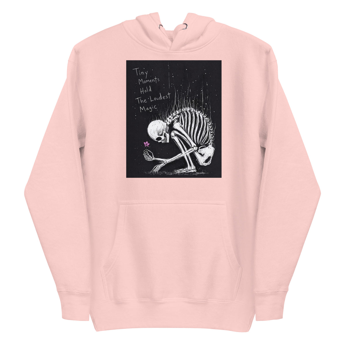 Light pink pullover hoodie with the 'Tiny Moments' goth graphic: a kneeling skeleton holding a tiny pink flower on a black background, with the words "Tiny moments hold the loudest magic"