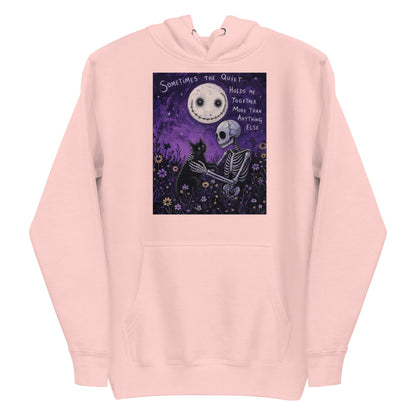 Light pink pullover hoodie with the 'The Quiet Heals' goth graphic: a skeleton and a black cat in a purple flower field under a smiling moon, with the words "Sometimes the quiet holds me together more than anything else"