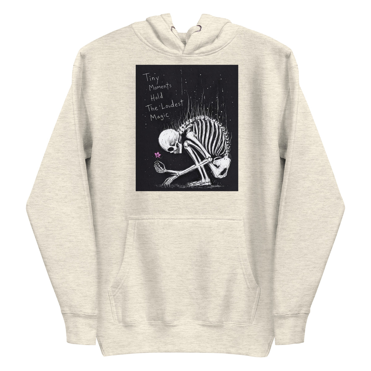 Oatmeal heather pullover hoodie with the 'Tiny Moments' goth graphic: a kneeling skeleton holding a tiny pink flower on a black background, with the words "Tiny moments hold the loudest magic"