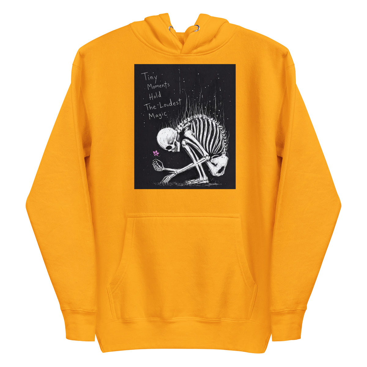 Gold pullover hoodie with the 'Tiny Moments' goth graphic: a kneeling skeleton holding a tiny pink flower on a black background, with the words "Tiny moments hold the loudest magic"