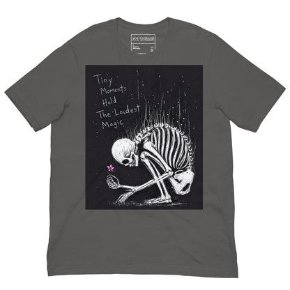 Asphalt unisex t-shirt with the 'Tiny Moments' goth graphic: a kneeling skeleton holding a tiny pink flower on a black background, with the words "Tiny moments hold the loudest magic"