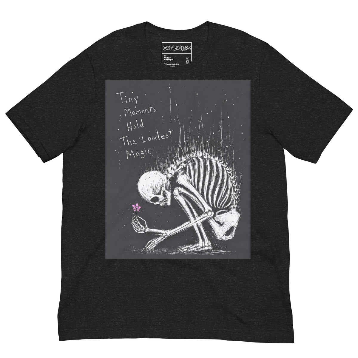 Black heather unisex t-shirt with the 'Tiny Moments' goth graphic: a kneeling skeleton holding a tiny pink flower on a black background, with the words "Tiny moments hold the loudest magic"