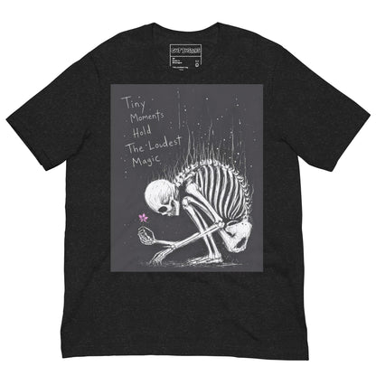 Black heather unisex t-shirt with the 'Tiny Moments' goth graphic: a kneeling skeleton holding a tiny pink flower on a black background, with the words "Tiny moments hold the loudest magic"