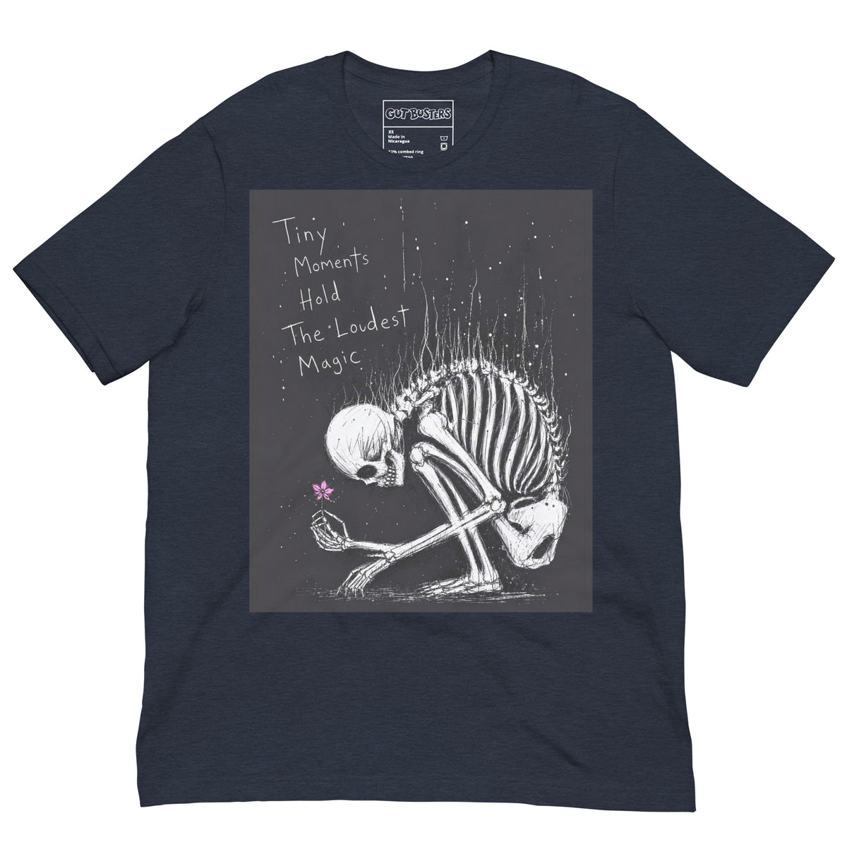 Heather navy unisex t-shirt with the 'Tiny Moments' goth graphic: a kneeling skeleton holding a tiny pink flower on a black background, with the words "Tiny moments hold the loudest magic"