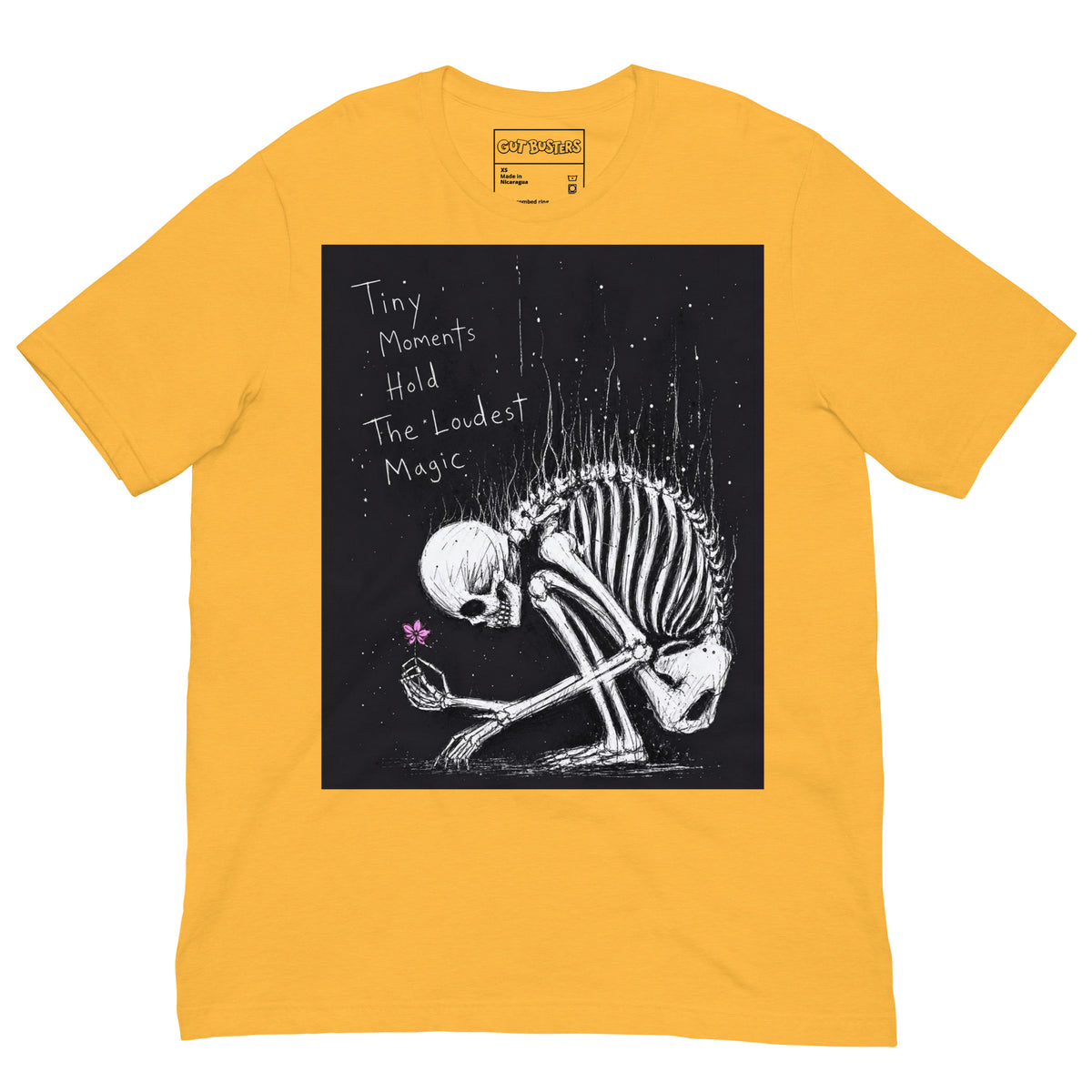 Heather yellow unisex t-shirt with the 'Tiny Moments' goth graphic: a kneeling skeleton holding a tiny pink flower on a black background, with the words "Tiny moments hold the loudest magic"