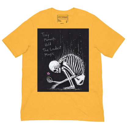 Heather yellow unisex t-shirt with the 'Tiny Moments' goth graphic: a kneeling skeleton holding a tiny pink flower on a black background, with the words "Tiny moments hold the loudest magic"