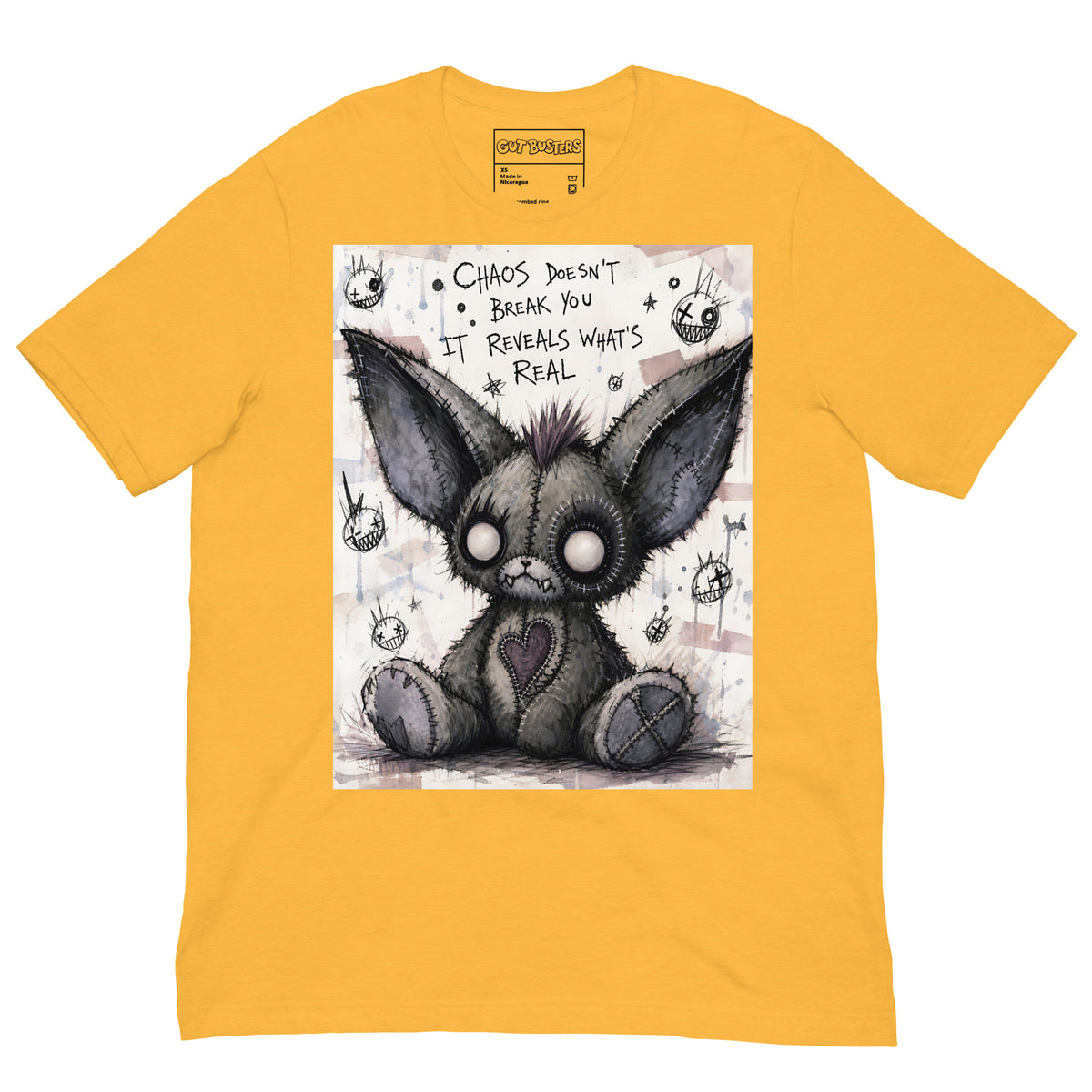 Heather yellow unisex t-shirt with the 'Chaos' goth graphic: a stitched gray big-eared creature with button eyes, with the words "Chaos doesn't break you, it reveals what's real"