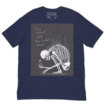 Navy unisex t-shirt with the 'Tiny Moments' goth graphic: a kneeling skeleton holding a tiny pink flower on a black background, with the words "Tiny moments hold the loudest magic"