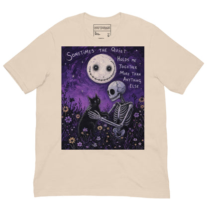 Soft cream unisex t-shirt with the 'The Quiet Heals' goth graphic: a skeleton and a black cat in a purple flower field under a smiling moon, with the words "Sometimes the quiet holds me together more than anything else"