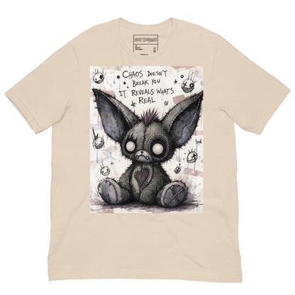 Soft cream unisex t-shirt with the 'Chaos' goth graphic: a stitched gray big-eared creature with button eyes, with the words "Chaos doesn't break you, it reveals what's real"