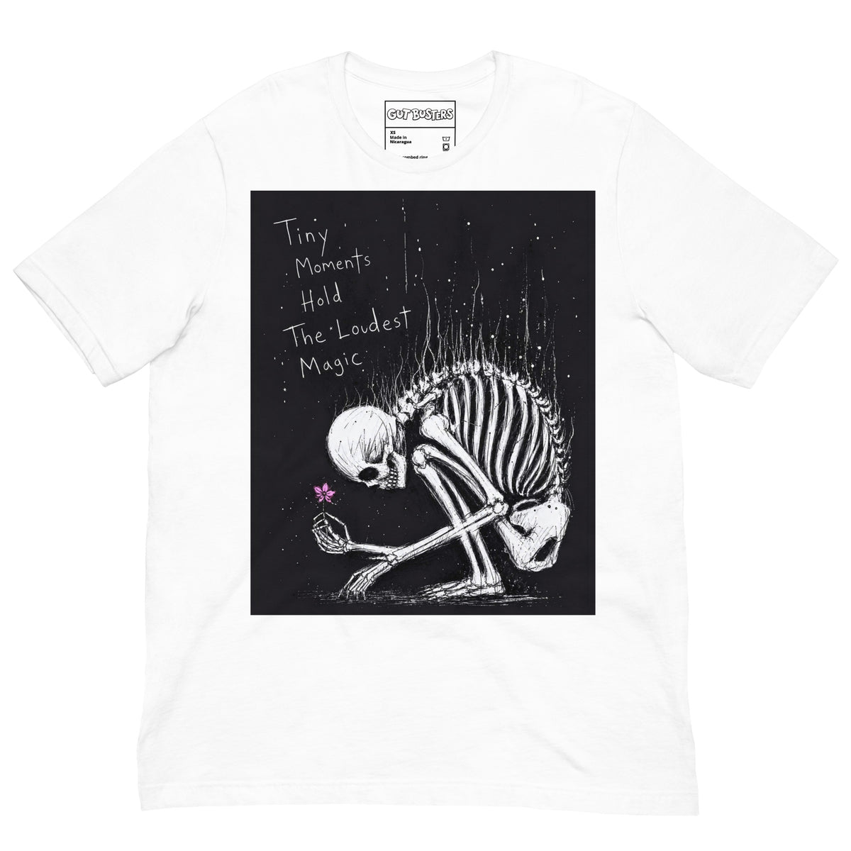 White unisex t-shirt with the 'Tiny Moments' goth graphic: a kneeling skeleton holding a tiny pink flower on a black background, with the words "Tiny moments hold the loudest magic"